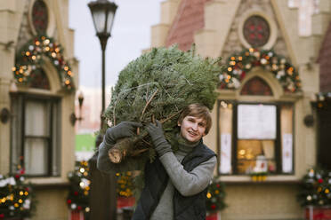 Smiling man with fir tree on his shoulder - EYAF00794