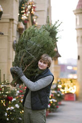 Smiling man with fir tree on his shoulder - EYAF00796