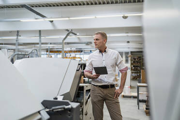 Businessman with a tablet in a factory looking around - DIGF09150