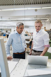 Two smiling colleagues using laptop in a factory - DIGF09156