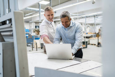 Zwei lächelnde Kollegen mit Laptop in einer Fabrik - DIGF09160