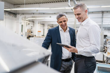 Two smiling businessmen looking at tablet in a factory - DIGF09172