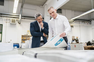 Two smiling businessmen discussing paper in a factory - DIGF09174