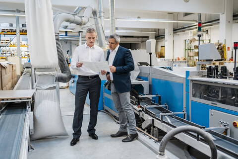 Two businessmen discussing paper in a factory stock photo