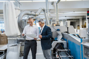 Two smiling businessmen discussing paper in a factory - DIGF09180