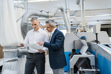 Two businessmen discussing paper in a factory - DIGF09181