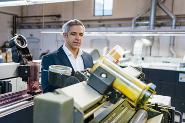 Geschäftsmann in einer Fabrik mit Blick auf eine Maschine - DIGF09201