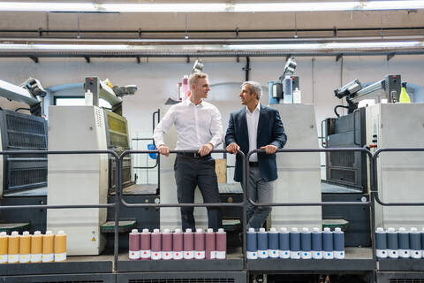 Zwei Geschäftsleute im Gespräch in einer Druckerei, lizenzfreies Stockfoto