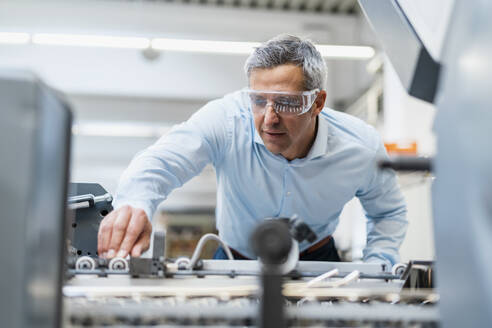 Man wearing safety goggles adjusting a machine in a factory - DIGF09238