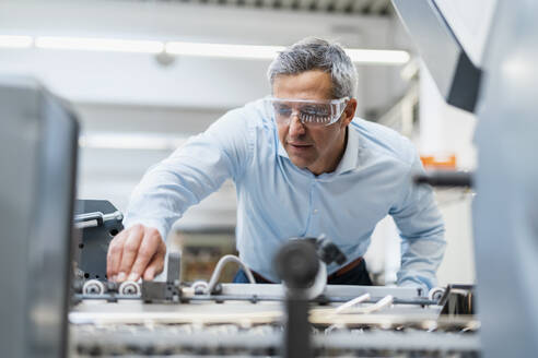 Mann mit Schutzbrille beim Einstellen einer Maschine in einer Fabrik - DIGF09238