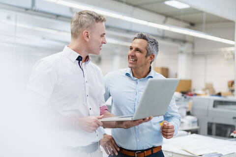 Zwei Kollegen benutzen einen Laptop und diskutieren in einer Fabrik, lizenzfreies Stockfoto