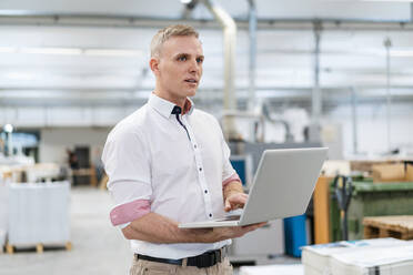 Businessman using laptop in factory - DIGF09248