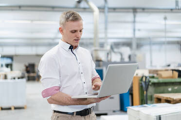 Businessman using laptop in factory - DIGF09249