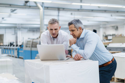 Zwei Kollegen benutzen einen Laptop und diskutieren in einer Fabrik, lizenzfreies Stockfoto