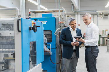 Zwei lächelnde Geschäftsleute mit Tablet im Gespräch in einer Fabrik - DIGF09275