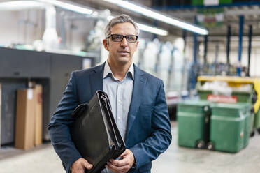 Portrait of a businessman with glasses and briefcase in a factory - DIGF09283