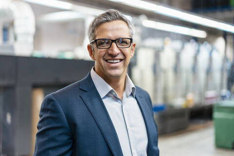 Porträt eines lächelnden Geschäftsmannes mit Brille in einer Fabrik, lizenzfreies Stockfoto