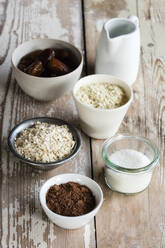 Zutaten für die Herstellung von Proteinkugeln (Kokosöl, Datteln, Hirseflocken, Haferflocken, Kokosraspeln und Kakaopulver) - EVGF03588