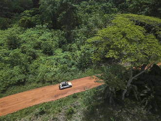 Elfenbeinküste, Korhogo, Luftaufnahme eines 4x4-Fahrzeugs, das auf einer unbefestigten Straße durch den grünen Dschungel fährt - VEGF01291