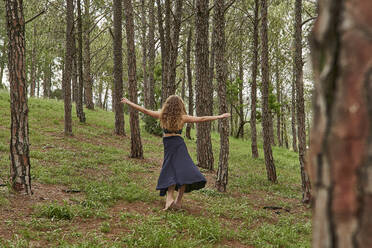 Rückenansicht einer barfuß tanzenden jungen Frau im Wald - VEGF01304