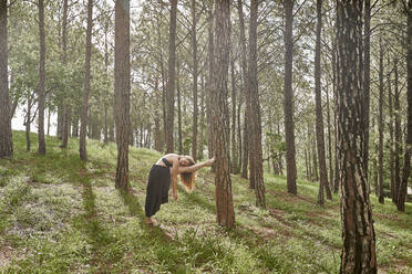 Barfüßige junge Frau bei Dehnungsübungen im Wald - VEGF01307