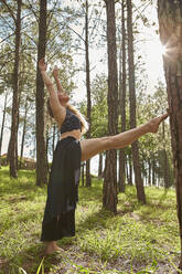 Barefoot young woman doing stretching exercise in the woods - VEGF01309