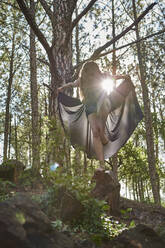 Barfüßige junge Frau steht auf einem Bein auf einem Felsen im Wald bei Gegenlicht - VEGF01315