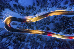 Italien, Provinz Sondrio, Livigno, Luftaufnahme von Fahrzeug-Lichtspuren auf kurvenreicher Bergstraße in der Abenddämmerung - WPEF02424