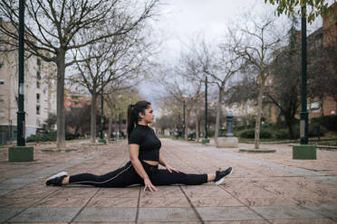 Young woman in black sportswear doing the splits on pavement - GRCF00022