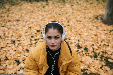 Porträt einer jungen Frau, die im Herbst mit Kopfhörern Musik hört - GRCF00026