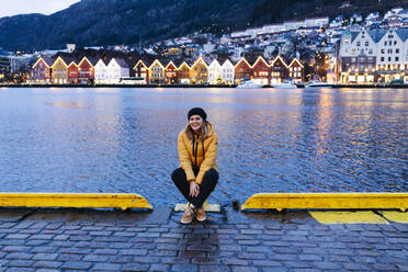 Frau mit gelber Jacke am Hafen in Bergen, Norwegen, sitzend - DGOF00006