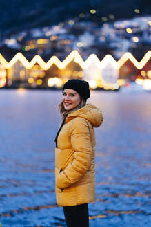 Frau mit gelber Jacke am Hafen in Bergen, Norwegen, sitzend - DGOF00007