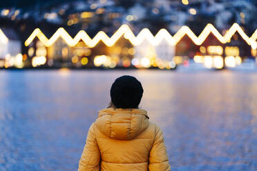 Rückansicht einer Frau in einer gelben Jacke am Hafen von Bergen, Norwegen - DGOF00008