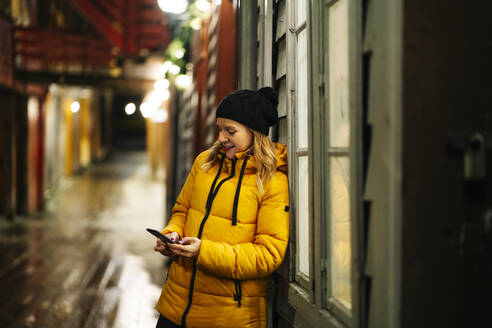 Frau in gelber Jacke und mit Smartphone in Bergen, Norwegen - DGOF00011