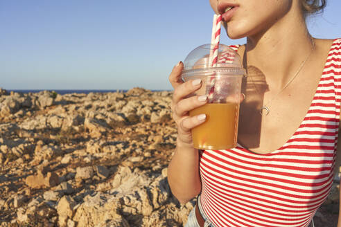 Junge Frau trinkt Saft am felsigen Strand - EPF00642