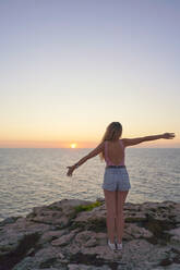 Young woman standing on cliff, watching sunset, rear view - EPF00654