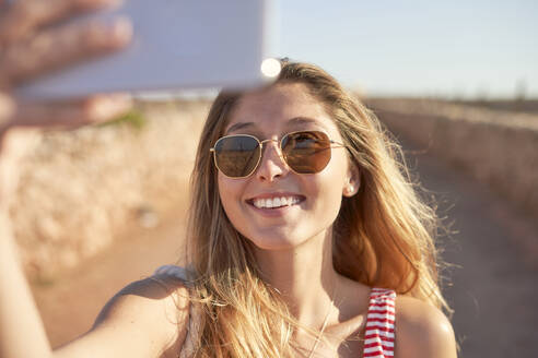 Lächelnde Frau mit Sonnenbrille, die ein Selfie bei Sonnenuntergang macht - EPF00657