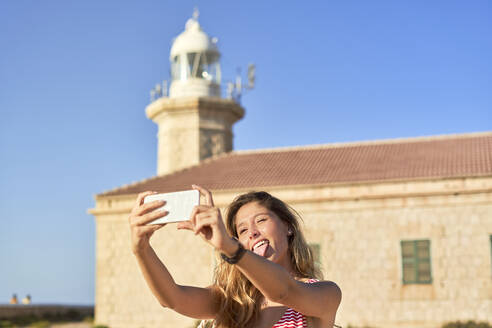 Junge Frau beim Fotografieren des Leuchtturms von Punta Nati, Menorca, Spanien - EPF00658