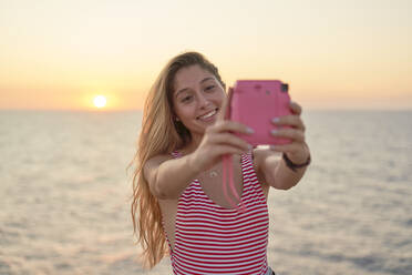 Young woman taking pictures of herself at sunset by the sea - EPF00677