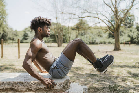 Junger Mann hebt die Beine beim Training auf einer Steinbank im Park, lizenzfreies Stockfoto