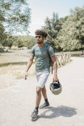 Junger Mann mit Helm geht im Park spazieren - FBAF01199