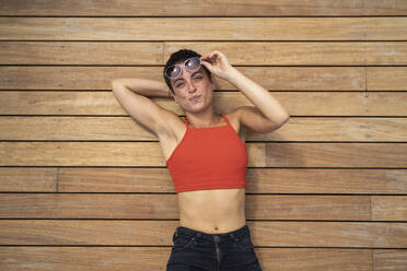 Porträt einer Frau mit Sonnenbrille, die auf dem Holzboden einer Terrasse liegt - FBAF01248