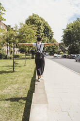 Back view of woman with backpack balancing on a wall - FBAF01255