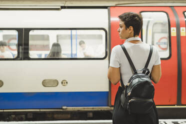 Rückenansicht einer Frau mit Rucksack, die auf dem Bahnsteig einer U-Bahn-Station wartet, London, UK - FBAF01258