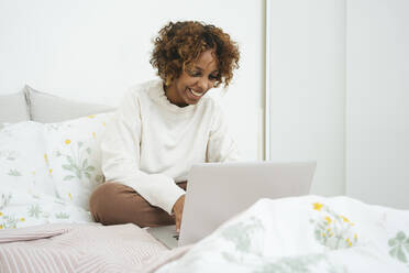 Happy young woman using laptop in bed at home - VPIF01918