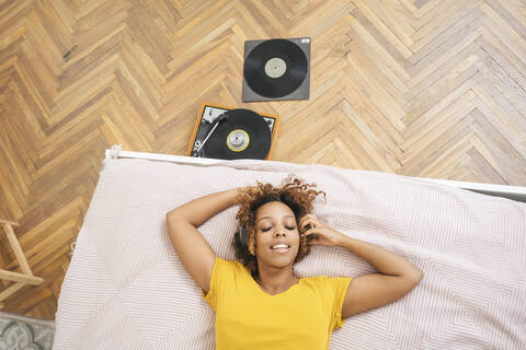 Young woman lying on bed listening to music with headphones and record player stock photo