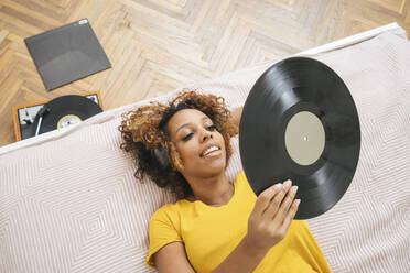 Junge Frau liegt auf dem Bett und hört Musik mit Kopfhörern und Plattenspieler - VPIF01934