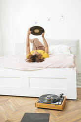Junge Frau liegt zu Hause auf dem Bett und hält eine Schallplatte - VPIF01935