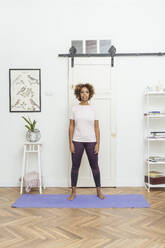 Young woman standing on yoga mat at home - VPIF01940