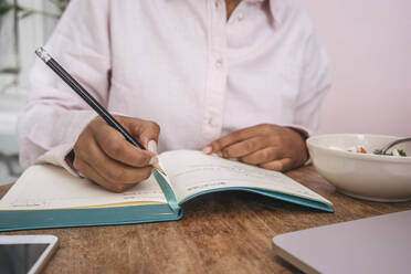 Close-up of young woman taking notes at table - VPIF01964